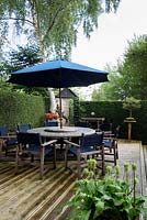 Dining area on raised decking at the end of the garden surrounded by a neatly clipped evergreen hedge 