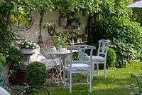 Old-fashioned bed, vintage chairs and table in front of house with 
pots and climbing plants