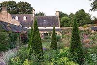 View through tightly clipped Taxus - Yew - pyramids with informal herbaceous
 planting beneath towards country house