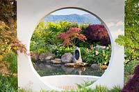 A Meditation Garden, looking through a contemporary representation of a 
Japanese moon gate to the focal stone sculpture on rocks above a pool. 
Planting includes Acer palmatum 'Shindeshojo', Acer palmatum
 'Dissectum Atropurpureum', Acer japonicum 'Vitifolium', Rodgersia aesculifolia and
Zantedeschia aethiopica