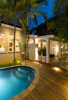 View at night showing decking with lighting, from swimming pool towards the 
house entrance with pots of Sanseveria