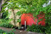 Contemporary water feature incorporating a waterfall, walls and metal sculpture, near a deck and 
surrounded by tropical foliage planting 