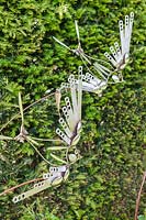 Birds and Bees - artwork made of steel cutlery - shown against a hedge
