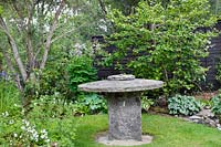 Old millstone used as a table, set in lawn surrounded by mixed beds
