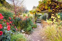 Sunken garden with Dahlia 'Bishop of Llandaff', Miscanthus, pennisetums, Prunus serrula and a vine covered dining area at Barn House, Chepstow, UK. 