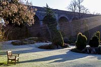 Rays of sunlight over frosty lawn and evergreen borders at Kilver Court, Somerset, UK. Designed by Roger Saul of Mulberry.