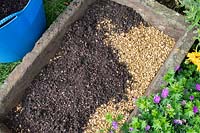 gritty compost mix over gravel in a stone sink, to be planted later with sempervivums.
