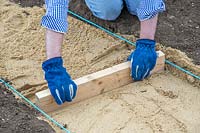 Man compacting and levelling gravel at base of path.