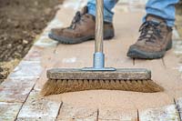 Man using broom to disperse kiln dried sand and fill gaps in newly laid pathway. 