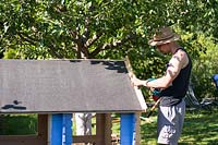 Man fixing the front panel of a blue painted playhouse. 