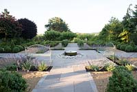 Formal garden with seating, central millstone water feature and topiary, overlooking countryside. 