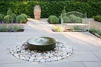 Formal garden with seating, central millstone water feature and topiary