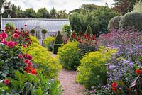 A brick path, leading through a restored Victorian walled kitchen garden to a greenhouse, is edged with clumps of Euphorbia ceratocarpa, interspersed with dahlias, asters, Verbena bonariensis and clipped bay trees.