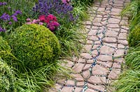 Pathway leading past border with clipped topiary balls and ornamental grasses. The Very Hungry Caterpillar Garden, RHS Tatton Park Flower Show, 2019.
