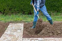 Man covering up the trench with newspaper, grass cuttings and manure with soil. 