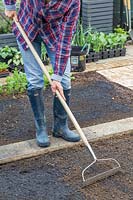 Woman using rake to mix in charcoal soil improver. 