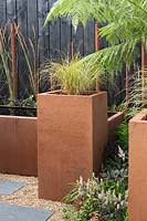 Anemanthele lessoniana in tall, rectangular Corten planter in a contemporary, urban style garden in 'The Penumbra' garden, RHS Tatton Park Flower Show 2018