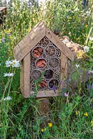 A small insect house is built in a flower meadow, in a wildlife friendly garden.