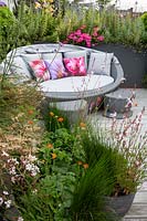 Roof terrace with wood decking and garden sofa with built in shade, with perennials and annuals forming a natural screen for privacy. Planting includes Gaura lindheimeri Whirling Butterflies, Juncus maritimus, Verbena bonariensis, Pink Bedding Geraniums, Olea europaea, Geum Totally Tangerine.