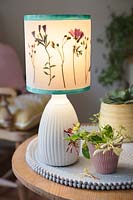 Upcycling an old plain lampshade with pressed flowers from the garden. Finished project with lampshade attached to a base on a table indoors