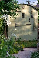 Brick path leading to a shepherds hut - The Naturecraft Garden, RHS Hampton Court Palace Flower Festival 2019