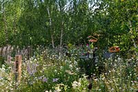 Bistro table and chairs set in a wildflower meadow, surrounded with birch trees and habitat houses. RHS Hampton Court Palace Flower Festival 2019.