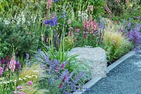Use of stone in the garden - a grey gravel path is neatly edged with a contemporary style white stonework and a large natural stone, with a border of colourful summer planting including Nepeta, Agapanthus, Digitalis, Salvia and Stipa tenuissima. RHS Hampton Court Palace Garden Festival 2019.Sponsor: Viking Cruises