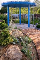 A garden designed to show how to cope with climate change. A rainfall pavilion with rain chains channels water into the garden. Large natural stones form a contemporary rock garden, with drought tolerant plants including Santolina, Lychnis coronaria 'Alba', at the RHS Hampton Court Palace Garden Festival 2019. Sponsor: Thames Water.