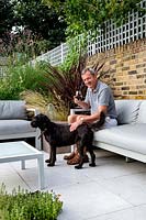 Man relaxing on sofa in outdoor room on patio, beside a pet dog
