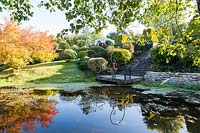 The landing with ornate hanging lanterns viewed from the Orekhovnitza river and reflected in the water. Acer ginnala with autumn colour on left. Orekhovno garden, Orekhovno, Pskov Oblast region, Western Russia.