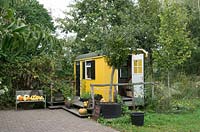 Bright yellow painted wooden site office near the entrance of the Mistletoe nursery with pumpkins ans vegetables for sale.