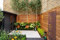 Small contemporary London garden with raised bed, bespoke garden seating with table and chairs and black wood garden room. 