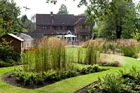 View from back of the garden looking towards the house, taking in island beds with grass paths. Shed, greenhouse and trampoline to one side
