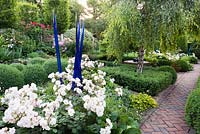 Rosa 'Penelope' - Rose - and blue glass sculpture with Betula - Weeping Silver Birch surrounded by clipped Buxus - Box. Herringbone brick path nearby 