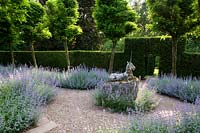 Sculpture in gravel pathway, nearby double border of Nepeta - Catmint - under row of Robinia. All against formal hedge with topiary arch
