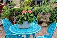 Garden designed by Nick Gough - blue table and chairs on patio with old saucepan container with Petunia Black Velvet and pink Pelargonium bedding.