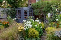 Small garden, planting includes: Phlox 'David', Achillea 'Moonshine', Stipa arundinacea, Helenium 'Moerheim Beauty' and Alchemilla mollis. House wall disguised by summerhouse, tree in large pot and mirror surrounded by trellis to create trompe l'oeil