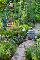 Watering can on paved path through herb and vegetable beds
