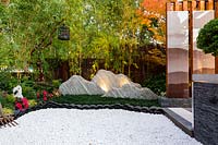 View of rocks representing a mountain range, across stepping stones. A green screen of golden bamboo and a dark brown bamboo fence.