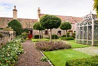 An aviary sits at the centre of the Upper Courtyard surrounded by Acer platanoides 'Globosum' and a chequerboard layout of alternating grass, sets, and blocks of planting including grasses, clipped evergreens and teucrium, at Broadwoodside, Gifford, East Lothian in September.