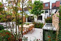 View of contemporary garden towards house in Wandsworth. With stone patio, seating and tables. With bespoke fitted barbecue.