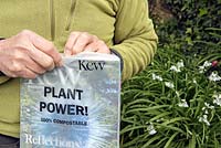Man opening the new 100 percent compostable wrapping or packaging of Kew magazine in his garden.