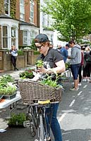 Lady putting plants into the wicker basket on a bicycle at Wilberforce Road plant sale