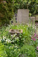 Gravestone and water trough among foxgloves, acquilegia and agapanthus in the The Evaders Garden at RHS Chelsea Flower Show 2015 - Sponsor: Chorley Council