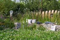 Cushions on curved dry stone bench backed with timber palisade surrounded by flowering perennials 
The BBC Spring Watch Garden  
RHS Hampton Court Festival  
Design: Jo Thompson in consultation with Kate Bradbury