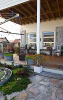 A path leading to a back verandah of a house with chairs, a table a clothes drying rack an old rusty steamer trunk and two retro galvanised tin washing tubs planted with Buffalo grass.