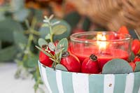 Table rrangement with red candle in strippy dish with rosehips and Eucalyptus foliage