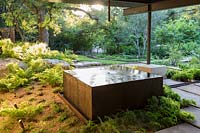 Square copper water feature near gravel bed with woodland beyond