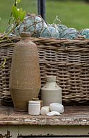 A collection of objects: earthenware bottles, a cane woven basket with glass fishing net floats, now used as decorative onraments