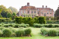 Beds of Miscanthus sinensis 'Kleine Silberspinne' and white Allium 'Mont Blanc' with screens of hornbeam, catmint, roses and blocks of clipped yew behind at Heale Garden, Wiltshire, UK. 
